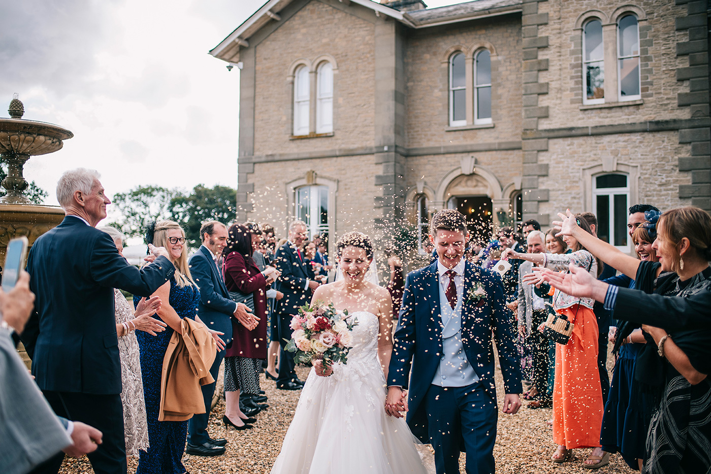 A bride and groom walking outside St Tewdrics whilst guest throw confetti