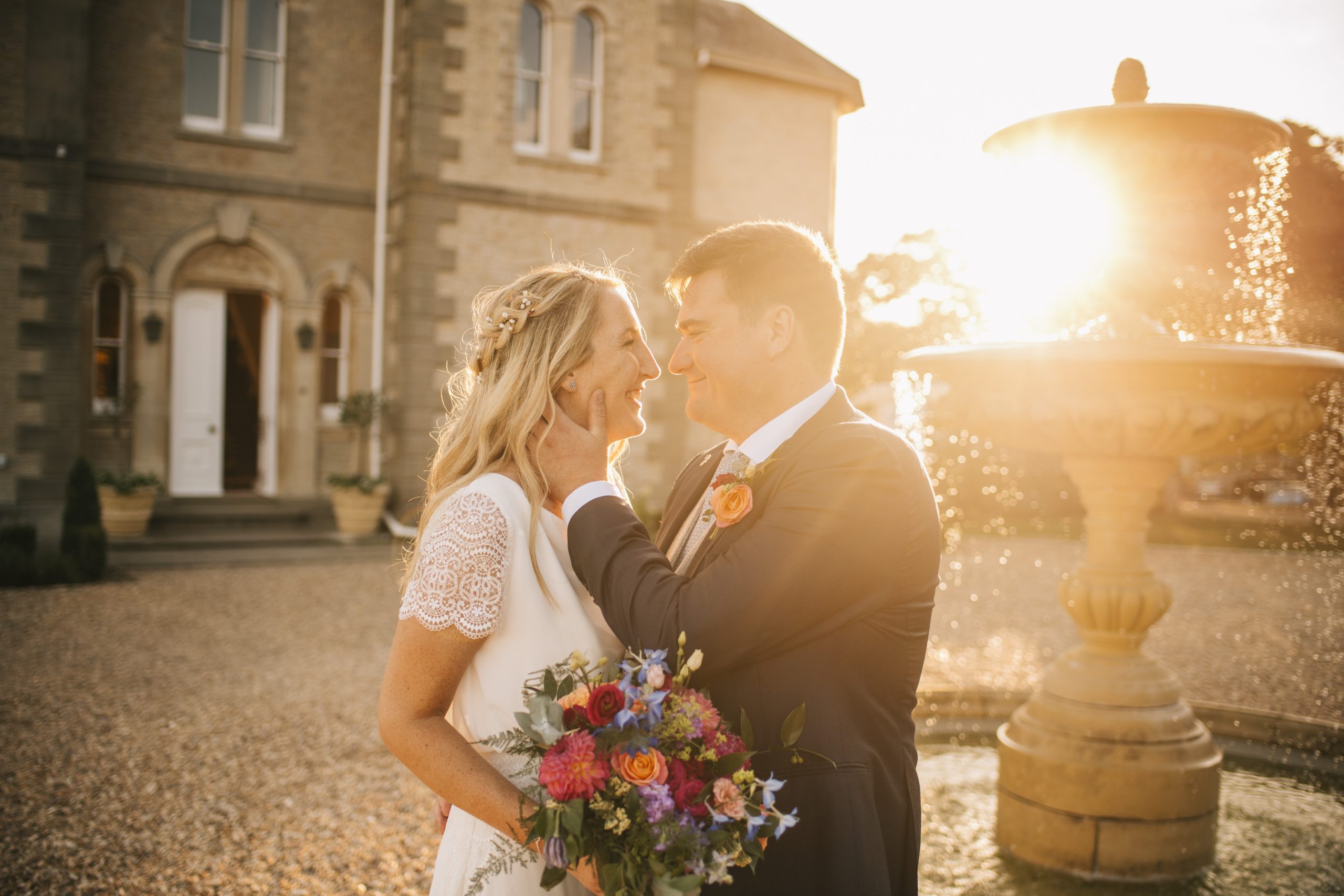 Bridge and Groom looking into each other's eyes smiling, his hand on her face, and St Tewdrics building in the background